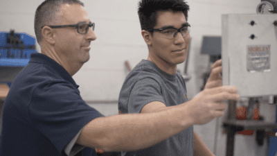 A manufacturing apprentice wearing safety glasses works with an instructor.