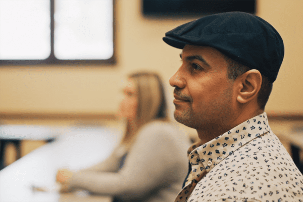 A middle aged Iraqi student sits in a classroom, listening to an instructor.